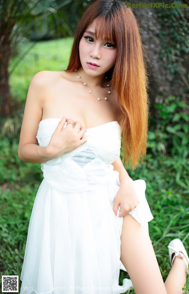 A woman in a white dress sitting in the grass.