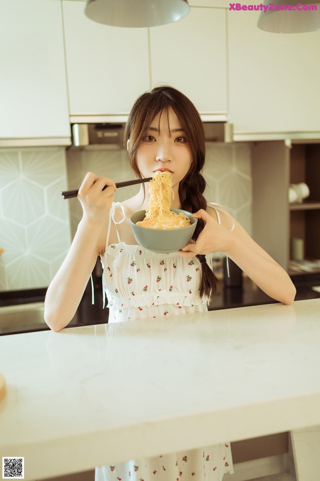 A woman eating a bowl of noodles with chopsticks.