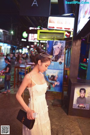 A woman in a white dress standing on a sidewalk.