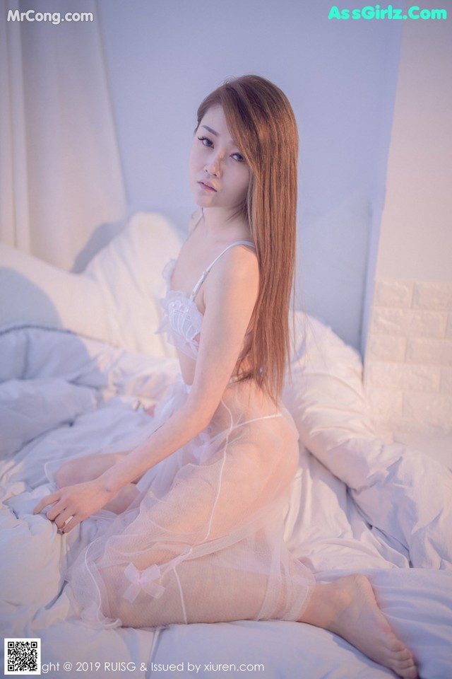 A woman in a white lingerie sitting on a bed.