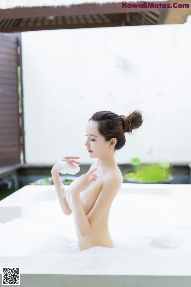 A naked woman sitting in a bathtub with foam on her body.