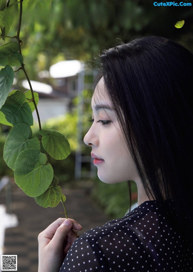 A woman holding a plant in front of her face.