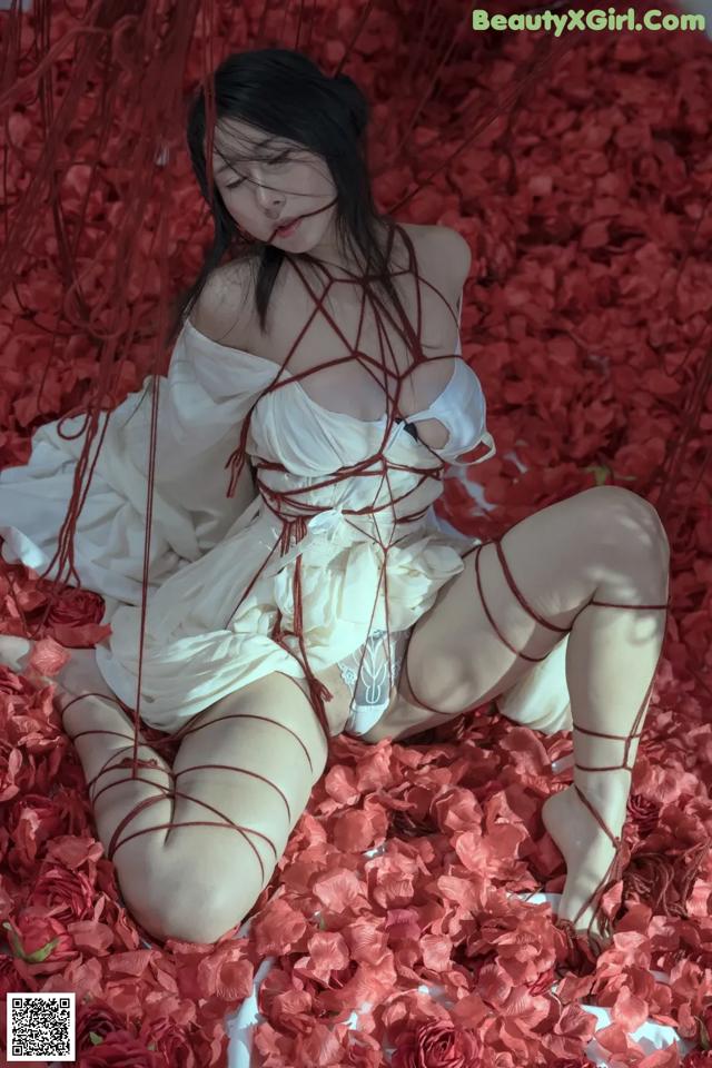 A woman in a white dress sitting on a bed of red roses.