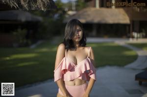 A woman in a black bikini standing on a wooden deck next to a pool.