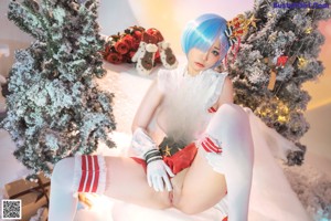 A woman in a white dress and red stockings posing in front of a Christmas tree.