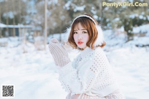 A woman in a white sweater and skirt standing in the snow.