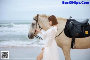 A woman in a white dress riding a horse on the beach.