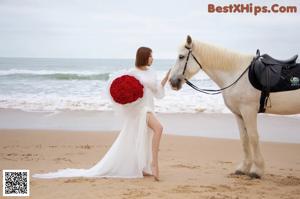 A woman in a white dress standing next to a white horse.