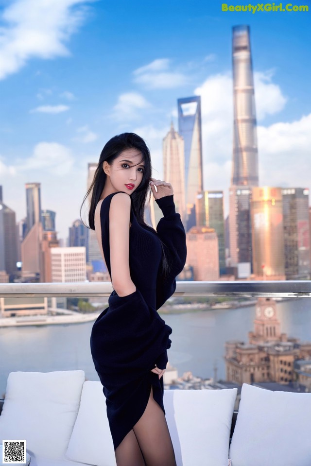 A woman in a black dress posing on a white couch.