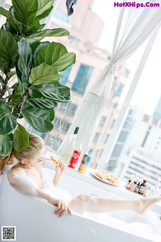 A woman sitting in a bathtub eating a piece of pizza.