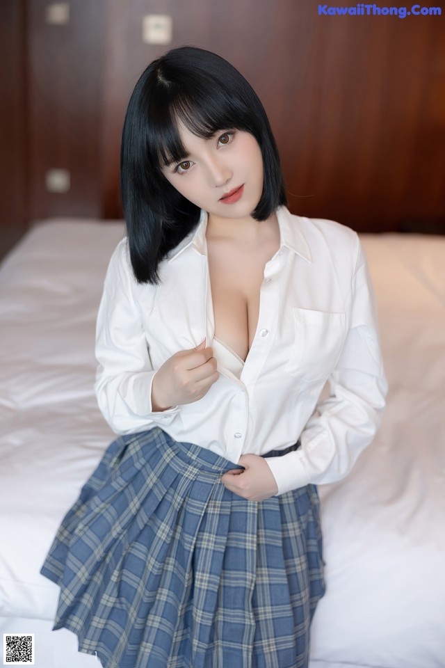 A woman in a white shirt and plaid skirt posing on a bed.