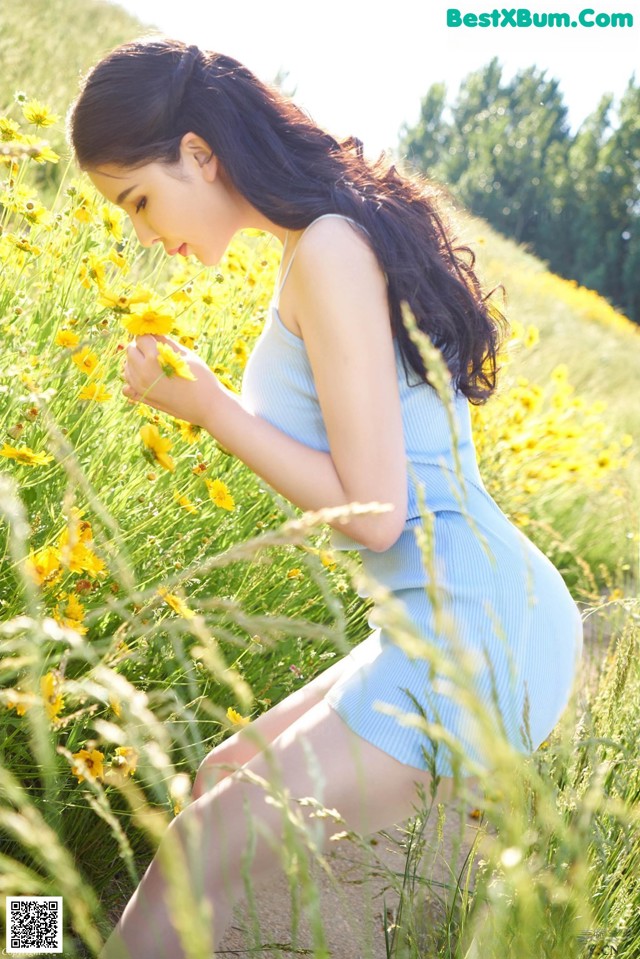 A woman in a blue dress sitting in a field of yellow flowers.