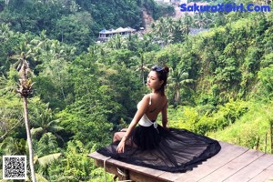 A woman sitting on a wooden platform in the middle of a lush green forest.