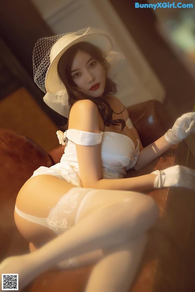 A woman in a white dress and hat sitting on a couch.