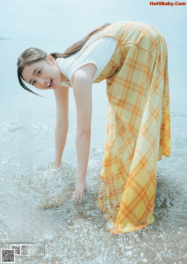 A woman in a yellow plaid skirt is standing in the water.