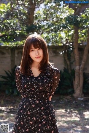 A woman in a black dress standing in front of a tree.