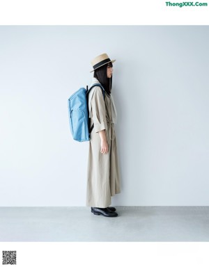 A woman in a blue raincoat leaning against a wall.