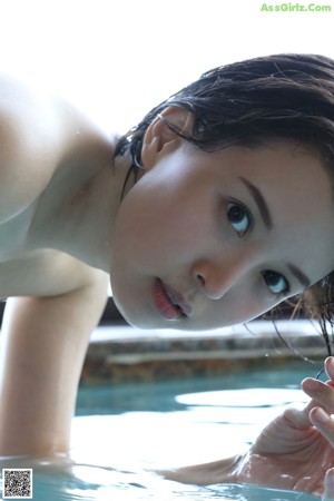 A naked woman sitting on the edge of a swimming pool.