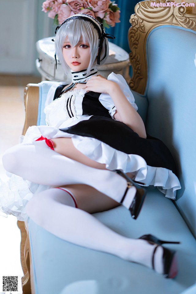 A woman in a maid outfit sitting on a blue chair.