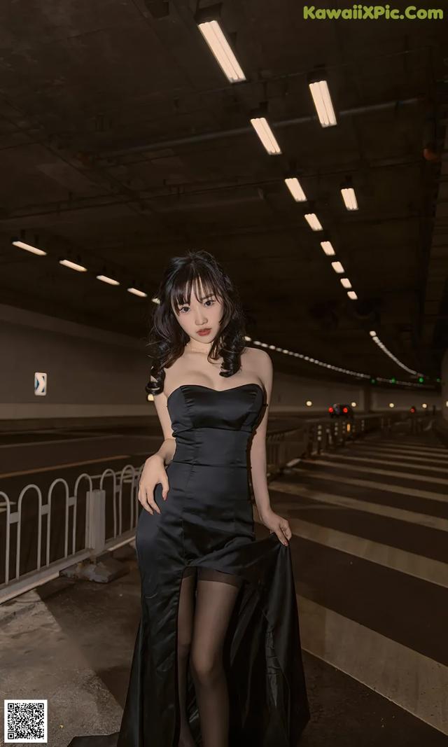 A woman in a black dress standing in a parking garage.