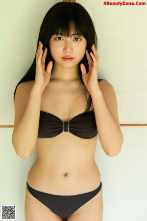 A woman in a black bikini sitting on a wooden bench.