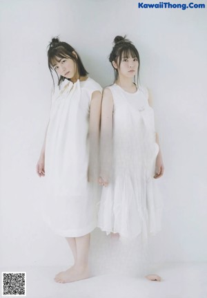 Two young women standing next to each other in white dresses.