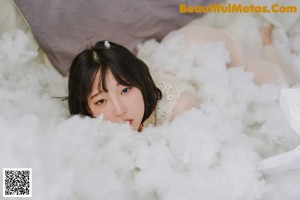 A woman in a white dress sitting on a bed covered in fluffy white clouds.