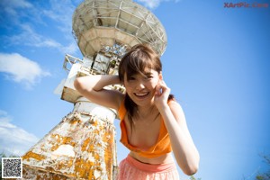 A woman standing in front of a large satellite dish.