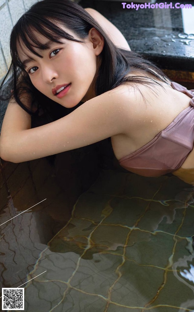 A woman in a pink bikini laying in a pool of water.