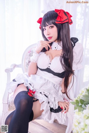 A woman in a maid outfit sitting on a wooden floor.