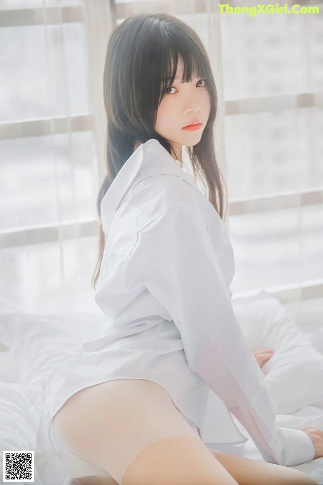 A woman in a white shirt and pantyhose sitting on a bed.