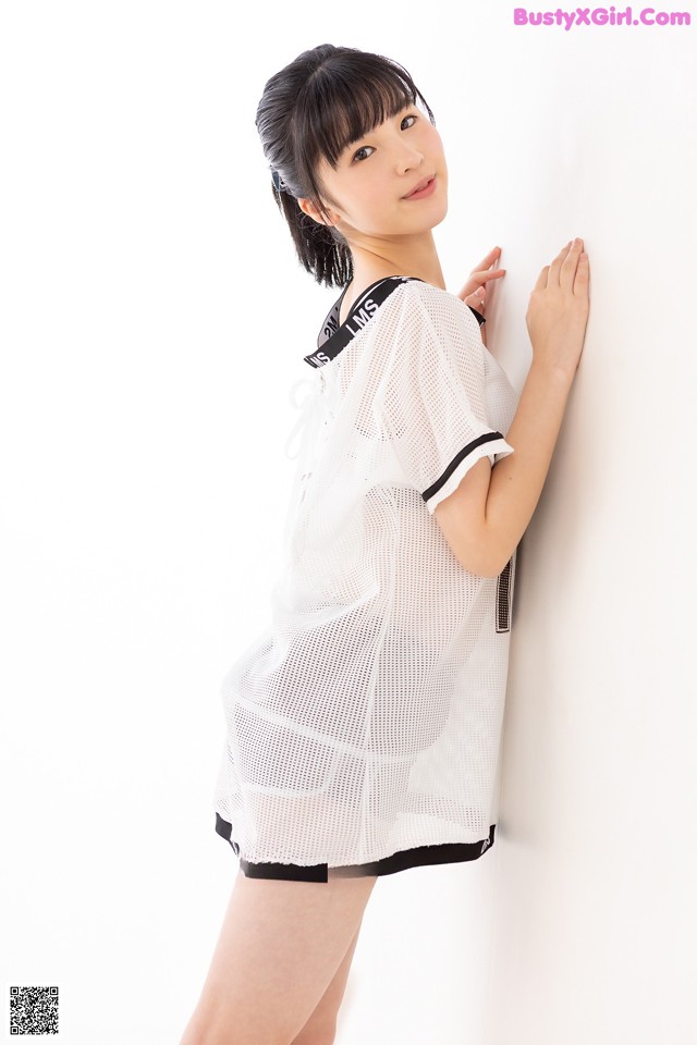 A woman in a white shirt and black shorts leaning against a wall.