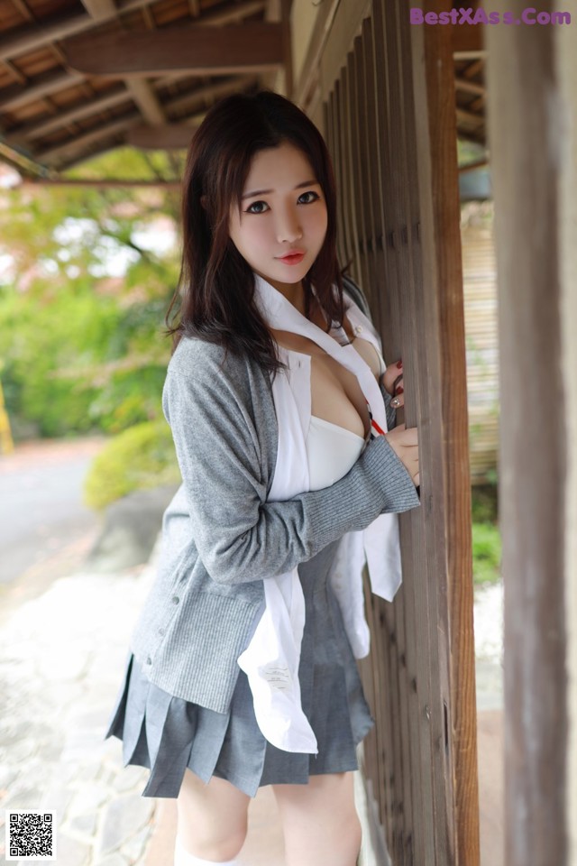 A woman in a school uniform leaning against a wall.