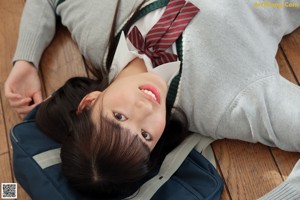 A young woman in a school uniform sitting on the floor.