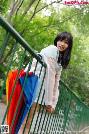 A woman sitting on a bench holding a rainbow colored umbrella.