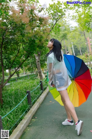 A woman in a white dress holding a rainbow colored umbrella.