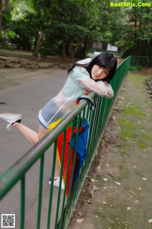 A woman sitting on a bench holding a rainbow colored umbrella.