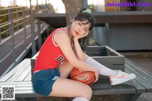 A woman in a red tank top and denim shorts holding a basketball.