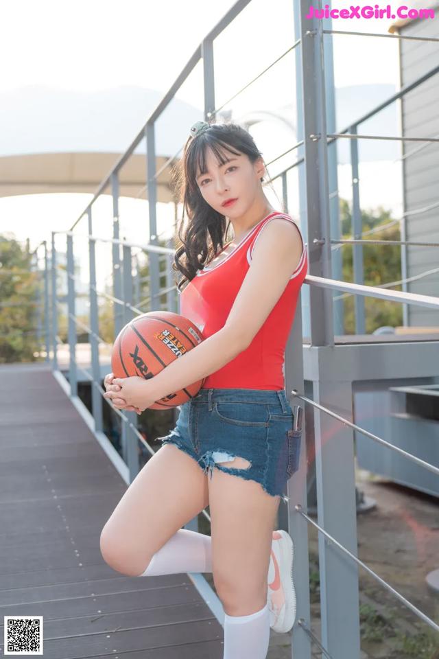 A woman in a red tank top and denim shorts holding a basketball.