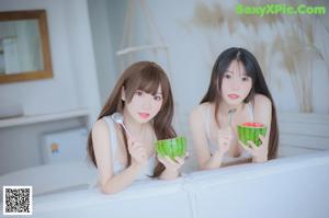 A couple of women sitting on top of a bed eating watermelon.