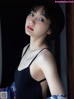 A woman in a black tank top leaning against a window.