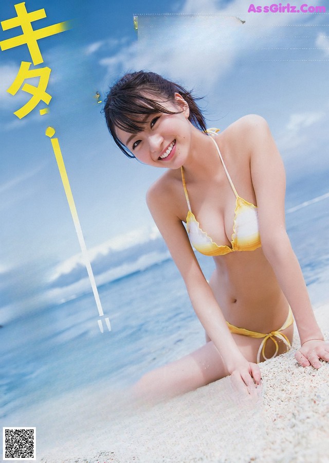 A woman in a yellow bikini sitting on the beach.